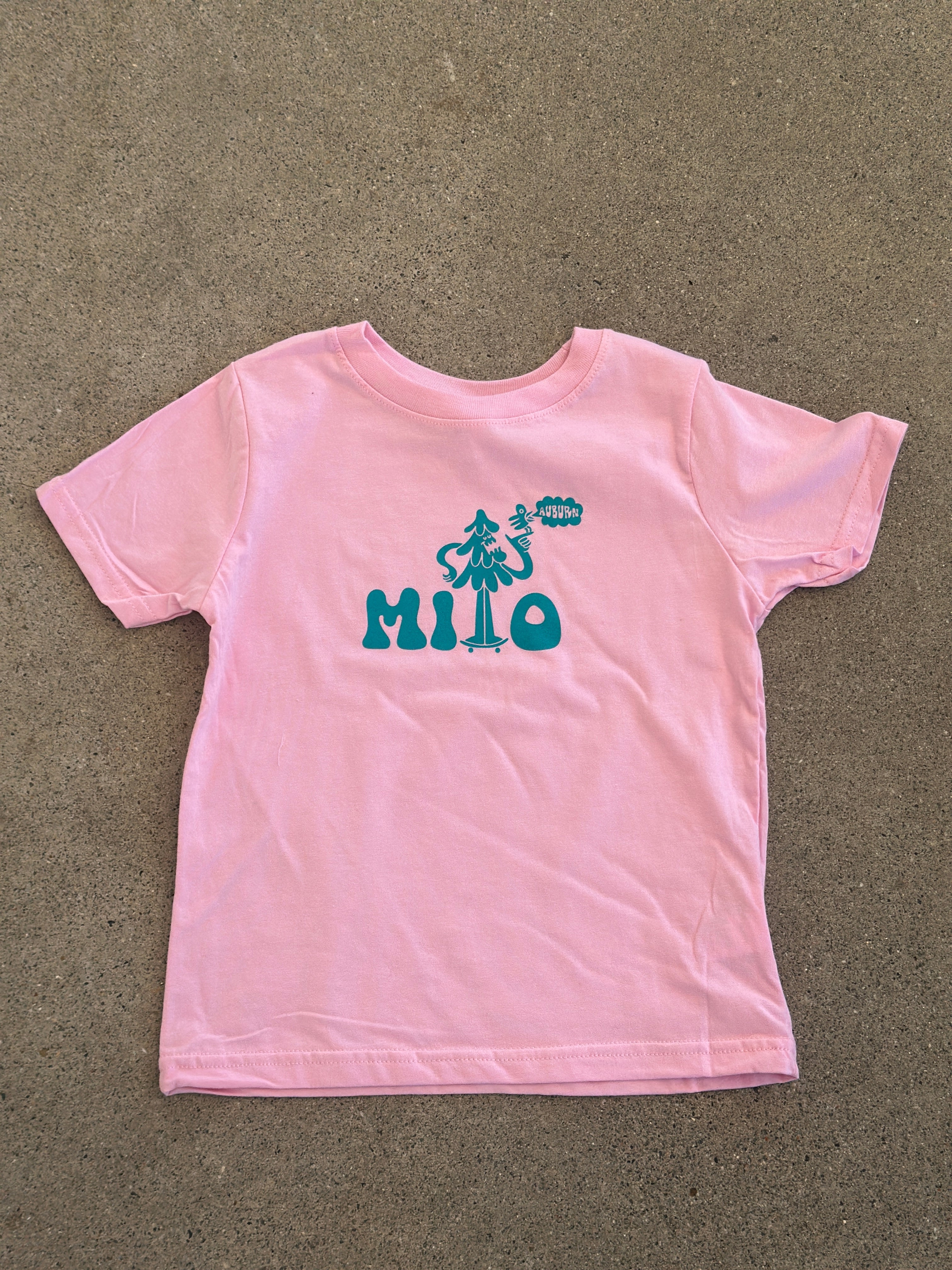 Pink sleeved top with teal text on a brown surface